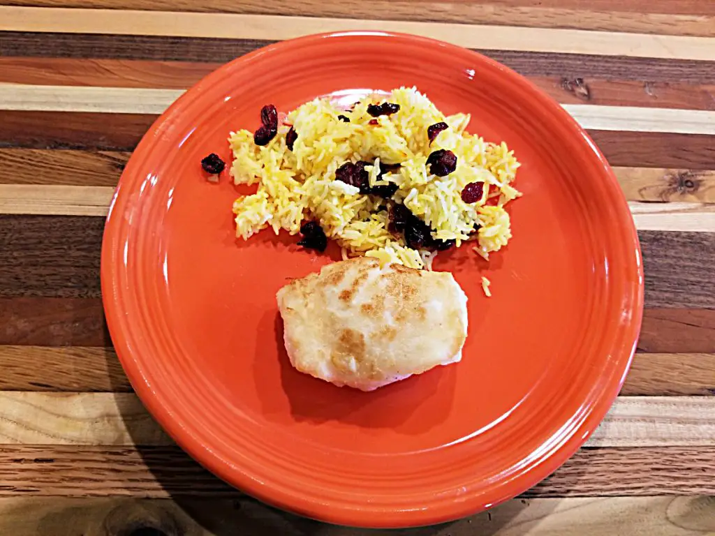 pan fried sea bass fillet on orange plate with side of saffron rice with dried cranberries